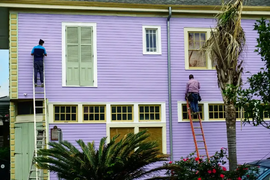 Two painters on ladders repainting the lap siding and trim of a coastal two-story home with palm trees, the type of exterior house painting project A Classic Touch Painting handles in New Smyrna Beach, FL.