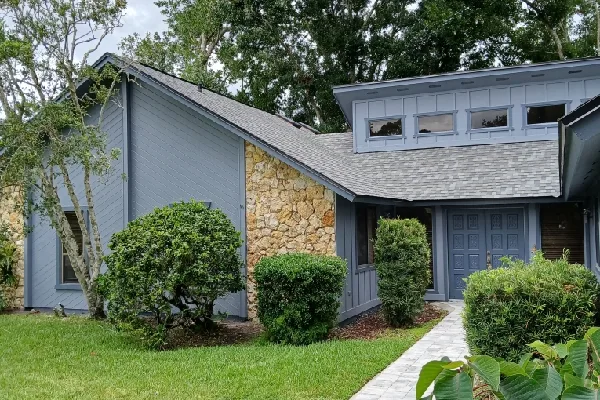 Gray-painted older home with a stone accent wall, shaded by mature trees and shrubs, the kind of shaded exterior that needs mildew treatment before house painting in DeLand, FL.