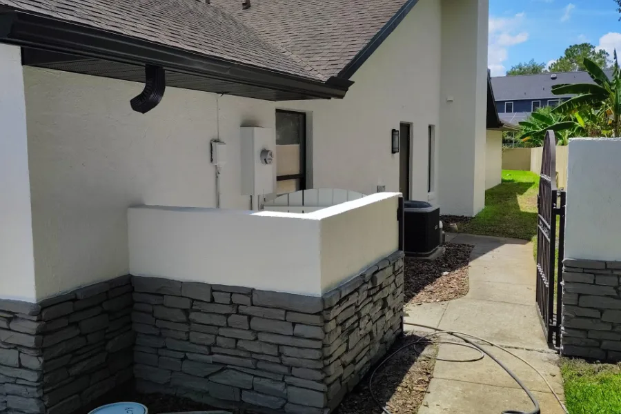Freshly painted white stucco walls above a gray stacked-stone base on a home exterior, showing a sealed stucco finish for house painting in Daytona Beach Shores, FL.